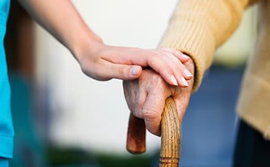 Elderly person with a cane being helped by someone else